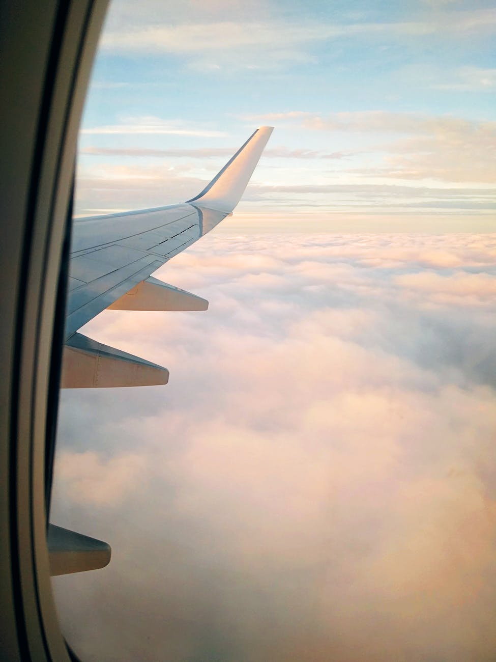 wing of aircraft flying over clouds at sundown